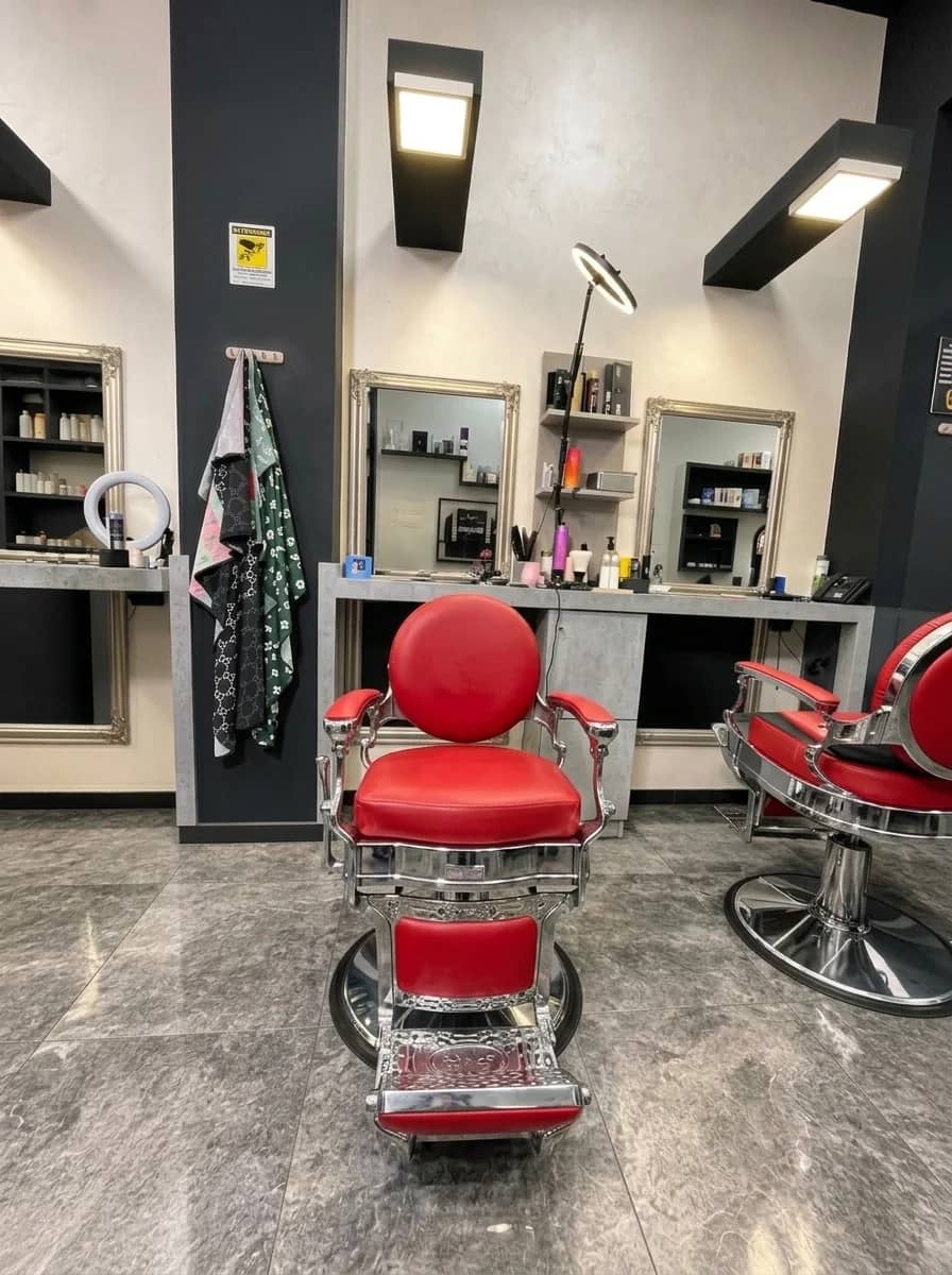 Una postazione del salone: poltrona da barbiere rossa davanti agli specchi con la cornice argento